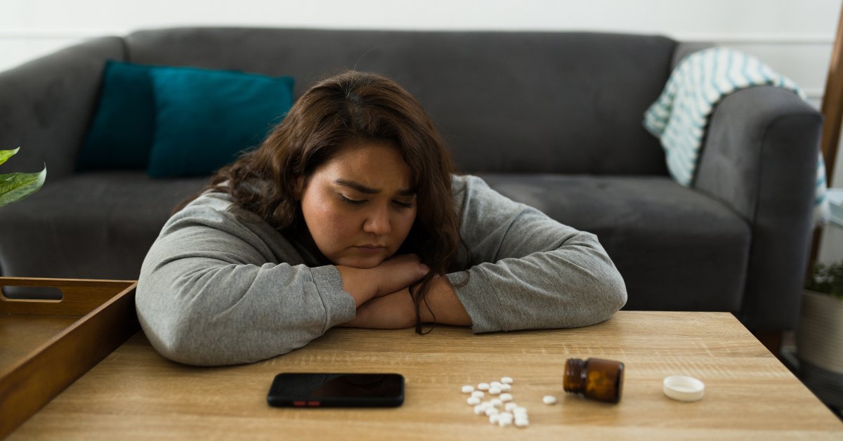 A woman reflecting with pills on the table, representing person-centered substance-use treatment support.