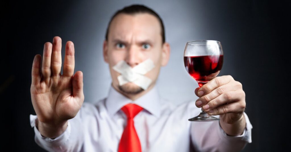 Man holding a glass of wine with a taped mouth and hand raised, illustrating how long it takes alcohol to leave your system.