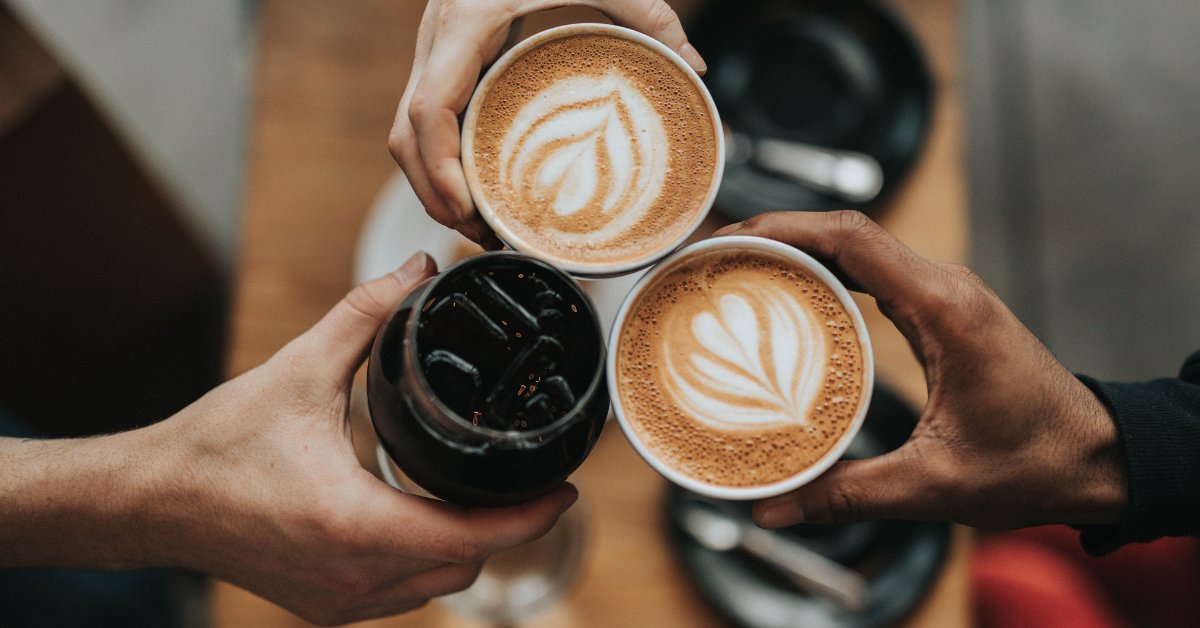 Hands holding cups of coffee and a glass, symbolizing the question: Is coffee a drug?