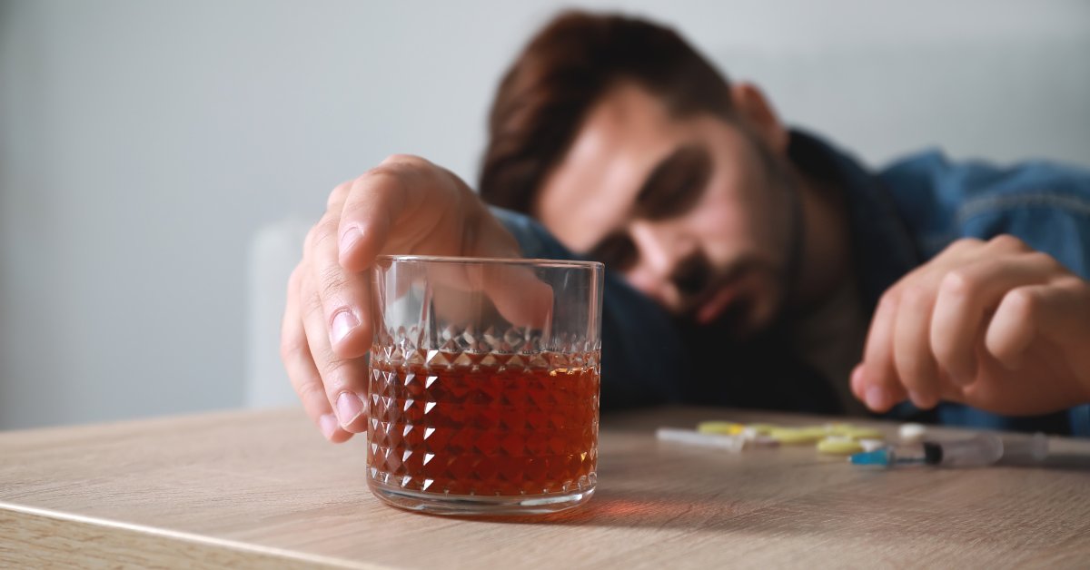 A man reaching for a glass of alcohol, symbolizing the link between alcohol addiction and dementia.