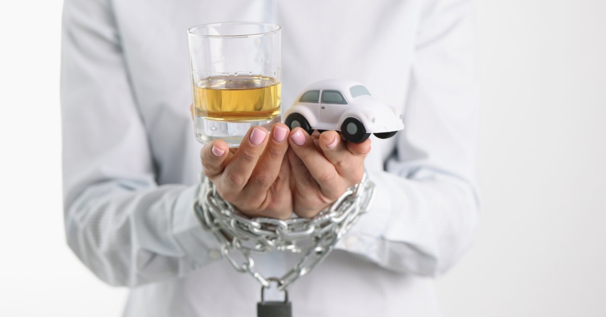 Hands in chains holding a glass of alcohol and a toy car, symbolizing the struggle of alcohol withdrawal.