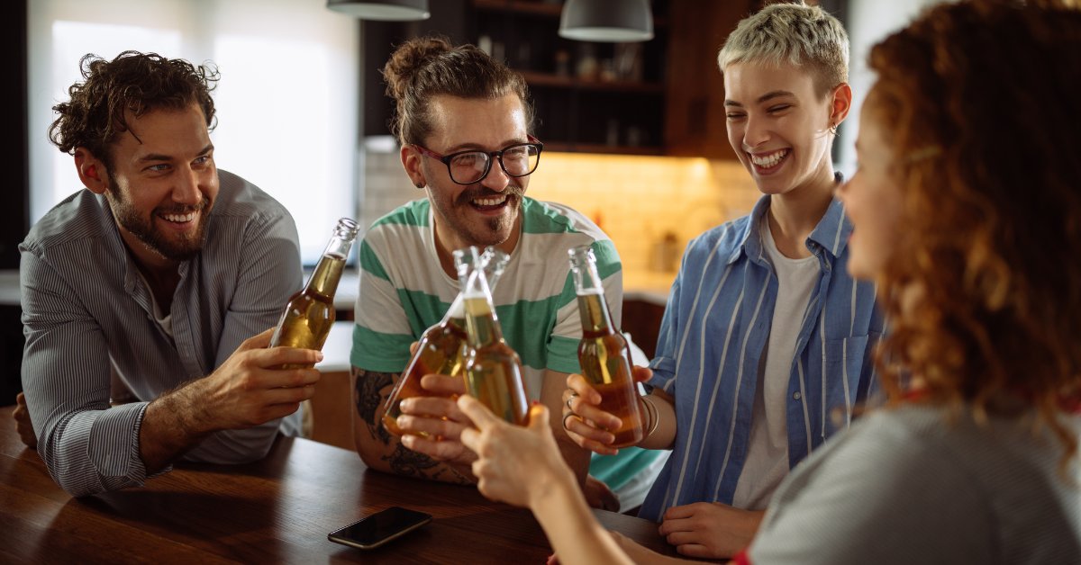 A group of friends cheerfully clinking beer bottles, representing the effects of drinking alcohol every day.