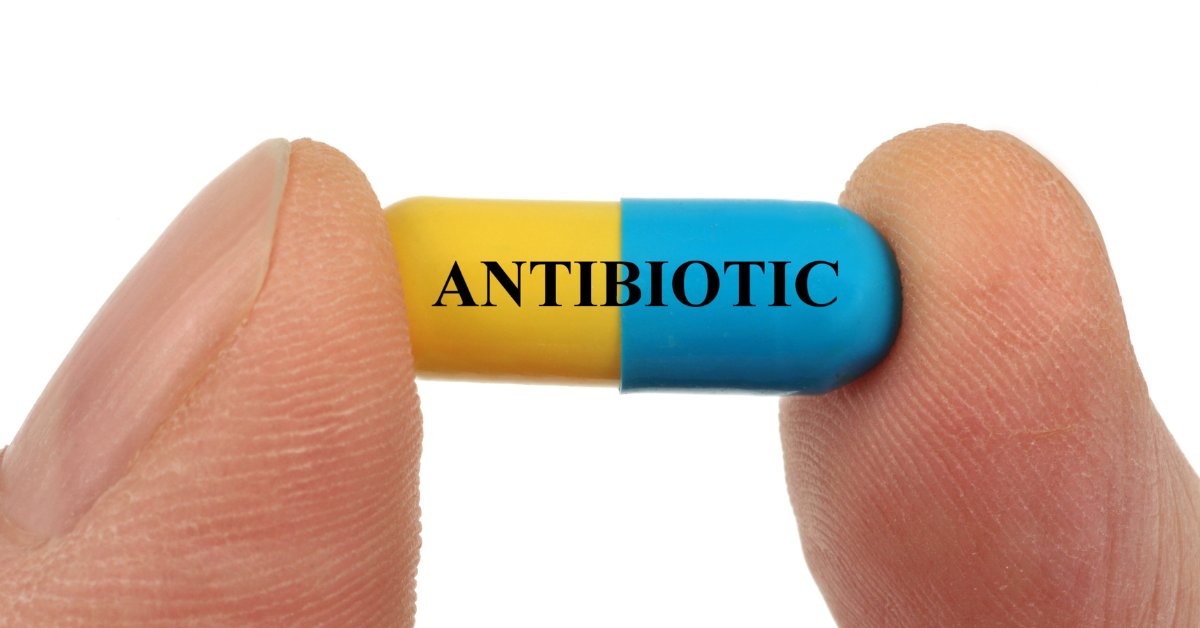 A close-up of a yellow and blue pill labeled "ANTIBIOTIC," symbolizing the interaction between antibiotics and alcohol.