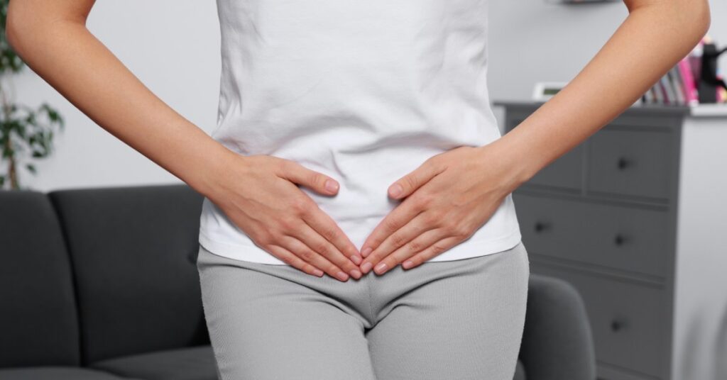 A woman holding her lower abdomen, symbolizing the question: Can alcohol consumption cause UTIs?