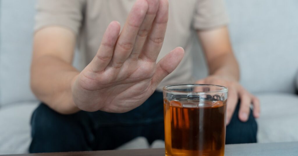 A person raising their hand to refuse a glass of alcohol, representing the concept of alcohol intolerance.